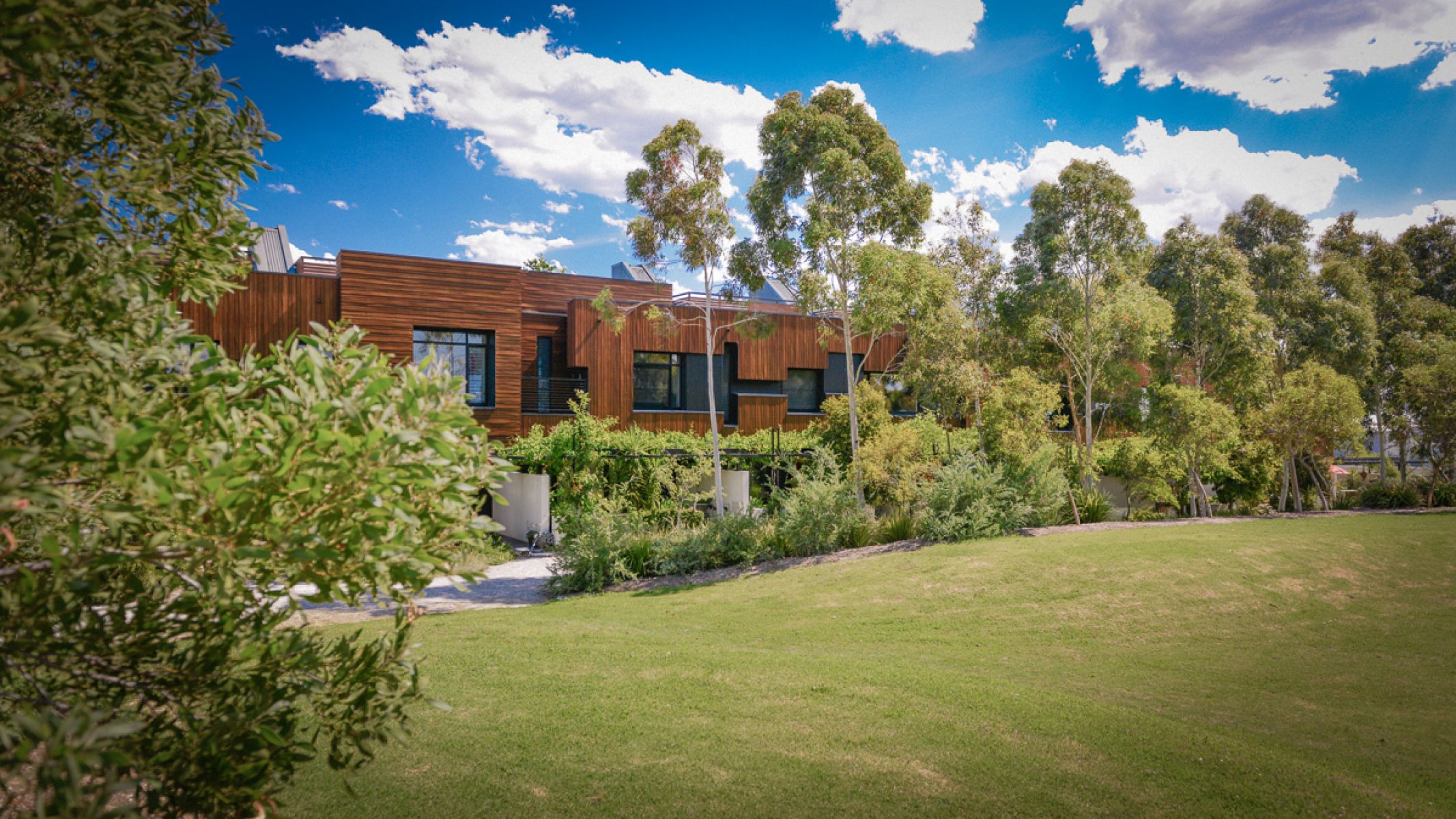 Photo of exterior of Heller Street complex. The building is in the distance and is situated next to a beautiful green space with trees. 
